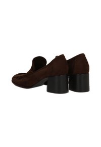 Mocasines de ante marrón con tacones cuadrados, puntas redondeadas, tacones bajos y diseño de tipo slip-on, mostrados desde ángulos trasero y lateral sobre fondo blanco.