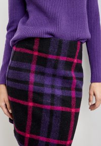 Maglione viola a maglia con texture a coste abbinato a una gonna nera con un motivo a quadri viola e fucsia. Tessuto morbido e design aderente.