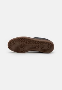 Svart sneakersåle med et strukturert gummimateriale. Har et heksagonalt mønster og en sirkulær aksent i midten.