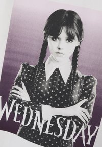 T-shirt blanc avec un graphique en noir et blanc d'une fille aux tresses, portant une robe noire à pois, et le mot "WEDNESDAY" affiché.