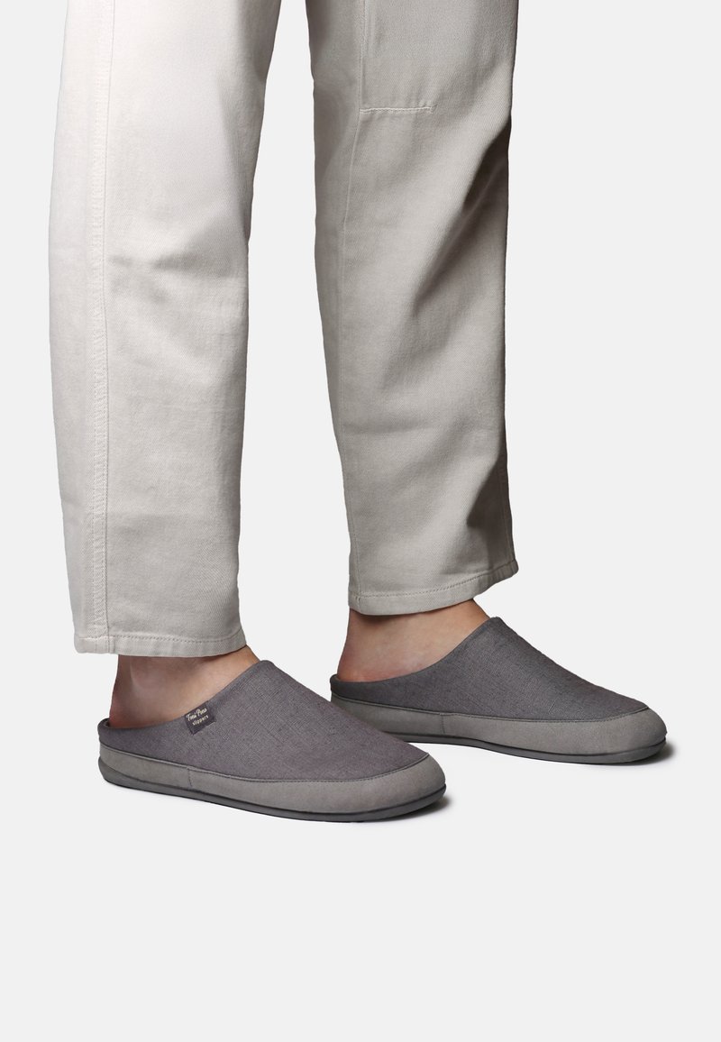 Piedi indossando pantofole slip-on grigie con suole spesse, abbinate a pantaloni casual beige su uno sfondo semplice.