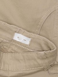 Lys brun stoff midjebånd med knappelukking og hvit metallring. Synlig søm og en jevn tekstur.