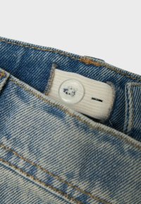 Farmer anyagú nadrág világoskék és sötétkék színátmenettel. Fehér textil címke és átlátszó gomb található a deréknál.