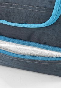 Grijze stoffen tas met blauwe ritsen, met een textuur oppervlak en een witte, zachte voering die zichtbaar is door een onafgebroken compartiment.