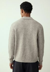 Hellgrauer, gerippter Strickpullover mit Schalkragen und langen Ärmeln, der eine lockere Passform und eine weiche Textur aufweist.