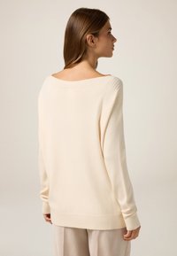 Pull beige surdimensionné avec un large col côtelé. Texture douce, manches longues et coupe ample, assorti à un pantalon rayé clair.