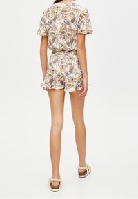 Dámský overall s květinovým vzorem z lehkého materiálu, s krátkými rukávy, volánkovým lemem a sandály s rozšířeným pasem. Nosit s béžovými sandály.