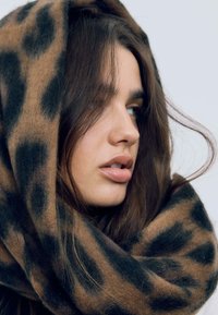 Smeđa i crna šal s uzorkom leoparda izrađen od mekog materijala, omotan oko vrata, s teksturiranim završetkom i hrabrim uzorkom.