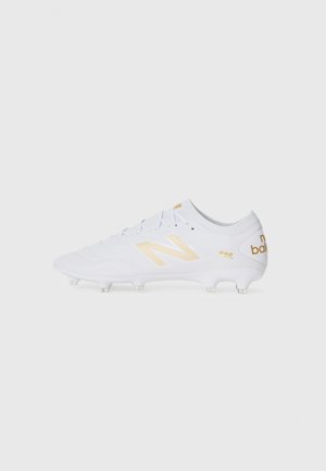 Chaussure de football blanche avec des accents dorés, présentant une tige texturée, un design épuré et un profil bas avec des crampons moulés pour une traction optimale.