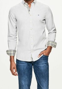Camicia grigia chiaro con bottoni, realizzata in un tessuto testurizzato, con polsini a scacchi verdi e blu navy e un piccolo logo ricamato sul petto.