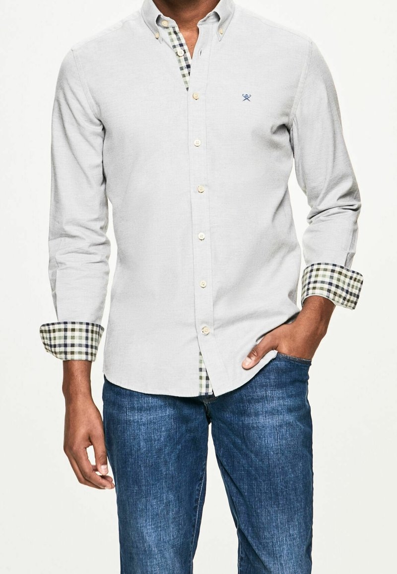 Camicia grigia chiaro con bottoni, realizzata in un tessuto testurizzato, con polsini a scacchi verdi e blu navy e un piccolo logo ricamato sul petto.