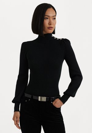 Zwarte geribde coltrui met lange pofmouwen, met decoratieve zilveren knopen op de schouder. Gecombineerd met donkere broek en riem.
