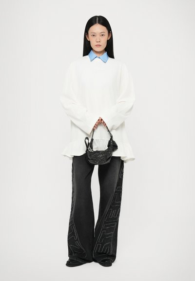 White oversized sweater with ruffled hem and blue collar, paired with black wide-leg pants featuring textured logos, and a small black handbag.