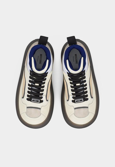 Pár bielych a béžových tenisiek Moschino s čiernymi šnúrkami, modrou vnútornou podšívkou a hrubými tmavosivými podrážkami, pohľad zhora.