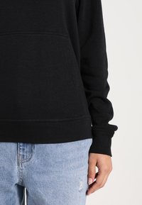 Svart sweatshirt med en framficka, ribbade muddar och nederkant. Kombinerad med ljusblå slitna jeans. Mjuk, bomullsmaterial.