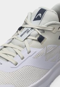 Αθλητικό παπούτσι ανοιχτού γκρι με λευκά κορδόνια, ύφασμα από δίχτυ και κείμενο «MOTION JR 1.5» στην γλωττίδα.