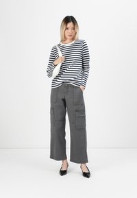Gestreiftes Langarmoberteil in Marineblau und Weiß, kombiniert mit weiteren grauen Cargo-Hosen mit seitlichen Taschen. Das Model trägt schwarze spitz zulaufende Ballerinas.
