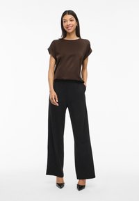 Brūns īsām piedurknēm tops, kas savienots ar augsto jostasvietu melniem platām biksēm. Tops ir ar gludu tekstūru, savukārt bikses ir ar pielāgotu piegriezumu.