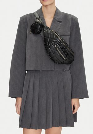 Persona che indossa un blazer grigio a righe sottili corto e una gonna a pieghe con una borsa a tracolla nera in pelle trapuntata e una piccola pochette.