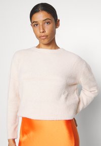 Helles rosafarbenes, flauschiges Sweatshirt mit Rundhalsausschnitt und langen Ärmeln, kombiniert mit einem orangefarbenen Satinrock. Weicher Stoff und lockere Passform.