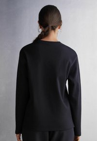 Langärmliges schwarzes Sweatshirt aus einer Baumwollmischung. Verfügt über einen Rundhalsausschnitt und ein lässiges Schnittdesign. Schlichte, klare Linien ohne Verzierungen.