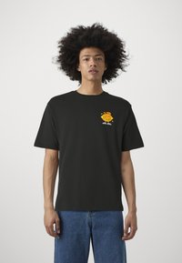 Camiseta de algodón negra de manga corta, con un gráfico colorido de "Lemon Stand" en el lado izquierdo del pecho. Ajuste casual con cuello redondo.