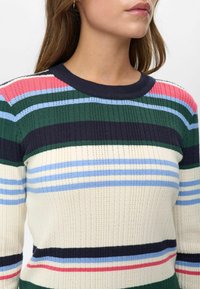 Pulover s črtasto rebrasto pletenino v kremni barvi, ki ima zelene, mornarsko modre, roza in modre črte. Okrogli izrez in podrobnosti teksturirane tkanine.