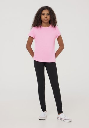 Maglietta rosa brillante a maniche corte, in misto cotone, abbinata a leggings neri, in cotone, con design aderente. Sneakers bianche con accenti rossi e blu.