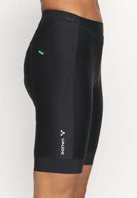 Lähikuva henkilöstä, joka käyttää mustia Vauden pyöräilyshortseja, joissa on logo reidessä ja pieni vihreä merkki sivusaumassa.