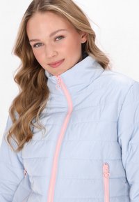 Giacca zip-up azzurro chiaro con accenti rosa, texture trapuntata, colletto alto e zip a forma di cuore. Presenta tasche laterali.