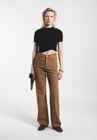 Camicetta nera a maniche corte abbinata a pantaloni marroni a vita alta e svasati. L'outfit presenta un design semplice e aderente con una texture liscia.