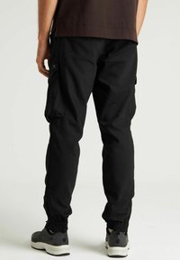 Pantalons cargo noirs avec des poignets élastiques et des poches latérales, en tissu durable, associés à des baskets grises. Vue montrant l'arrière.