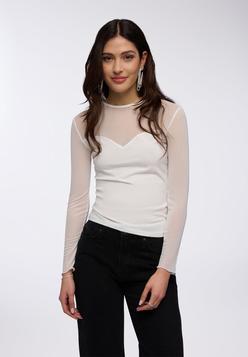 Top bianco a maniche lunghe con yoke in rete trasparente e scollatura a V, abbinato a pantaloni neri a vita alta. Design semplice e aderente.