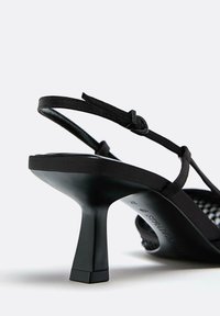 Czarne sandały na wysokim obcasie z cienkim paskiem, z kwadratowym obcasem blokowym i satynowym wykończeniem. Zauważalne detale to regulowany pasek wokół kostki.