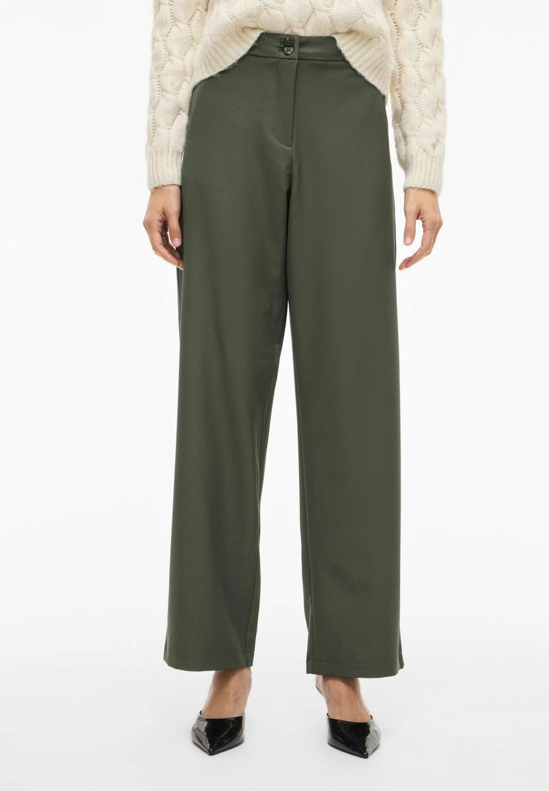 Olijfgroene broek met wijde pijpen, een gladde stof, een hoge taille met een knoop aan de voorkant en zijzakken, gecombineerd met zwarte puntige schoenen.