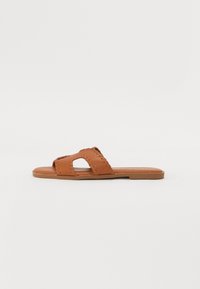 Brune lærskli sandal med åpen tå design, dekorativ søm og flat såle. Enkel, uforfalsket form.