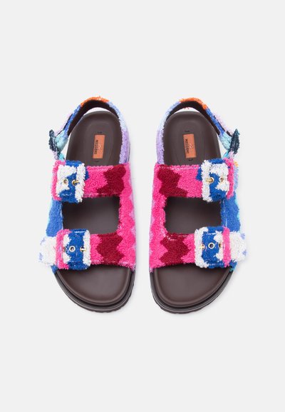 Πέδιλα με ανοιχτά δάχτυλα και ρυθμιζόμενους ιμάντες με αγκράφες, από πολύχρωμο πετρούτ ύφασμα και σκούρες καφέ σόλες, εμφανιζόμενα από πάνω.