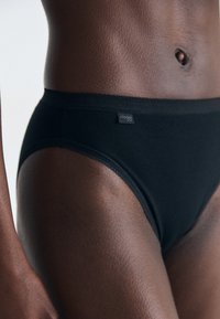 Black cotton brief with high waist; smooth texture and subtle stitching detail. Brand label visible on the side.