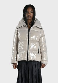 Doudoune en beige brillant avec un large col, dotée de coutures diagonales, d'une fermeture éclair à l'avant et de poches latérales. Fini texturé.
