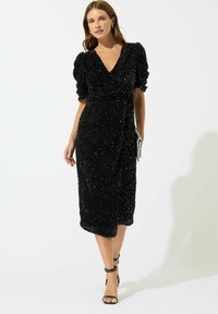 Svart paljettklänning med djup V-ringning, puffärmar och knälång nederkant. Har en texturerad yta och en omlott-design.