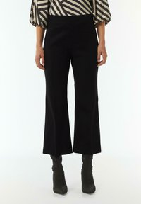 Zwarte wijde broek van gladde stof, met een hoge taille en een strakke snit, gecombineerd met strak passende zwarte enkellaarsjes.