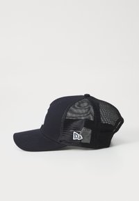 Svart baseballcaps med solid frontpanel og mesh bak. Har en hvit logo på forsiden og en sydd detalj på siden.
