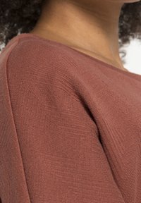 Haut en tricot de couleur rouille, texturé, avec un col large et des détails au niveau des coutures d'épaule, fabriqué dans un tissu doux et léger.