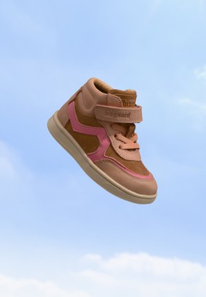 Baskets montantes marron et rose pour enfants avec bande et lacets flottant sur un fond de ciel bleu.