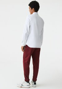 Cămașă albă cu mâneci lungi asociată cu pantaloni joggers vișinii și adidași albi. Cămașa are guler, iar pantalonii joggers au manșete elastice.