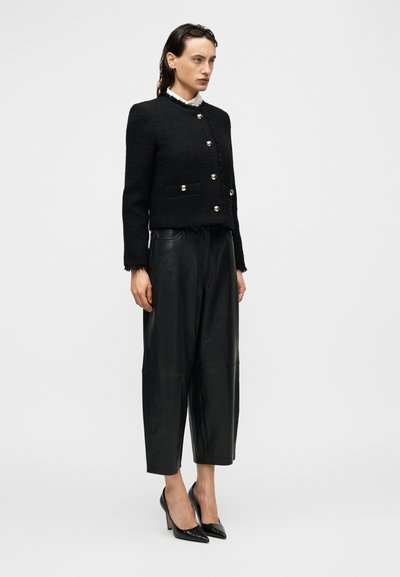 Μαύρο cropped σακάκι με υφή και χρυσά κουμπιά, σε συνδυασμό με φαρδιά μαύρα δερμάτινα παντελόνια και γυαλιστερά μαύρα τακούνια με μυτερή μύτη.