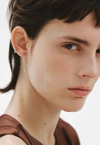 Pendientes de plata con un diseño de cadena y una pequeña gema decorativa, combinados con un pendiente de aro dorado minimalista en la oreja izquierda.