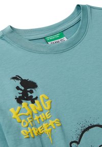 Světle modrý dres s výstřihem a černým kresleným králíkem, na hrudi vyvýšený žlutý text "KRÁL ULICE" ve stylu graffiti.