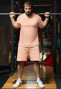 T-shirt de sport pêche à manches courtes avec short assorti, présentant une coupe décontractée, une texture lisse et un petit détail de logo. Baskets blanches.