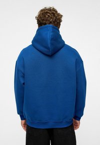 Hoodie bleu avec une grande capuche, fabriqué en tissu doux. Présente une coupe décontractée, des poignets côtelés et un ourlet droit, vu de dos.